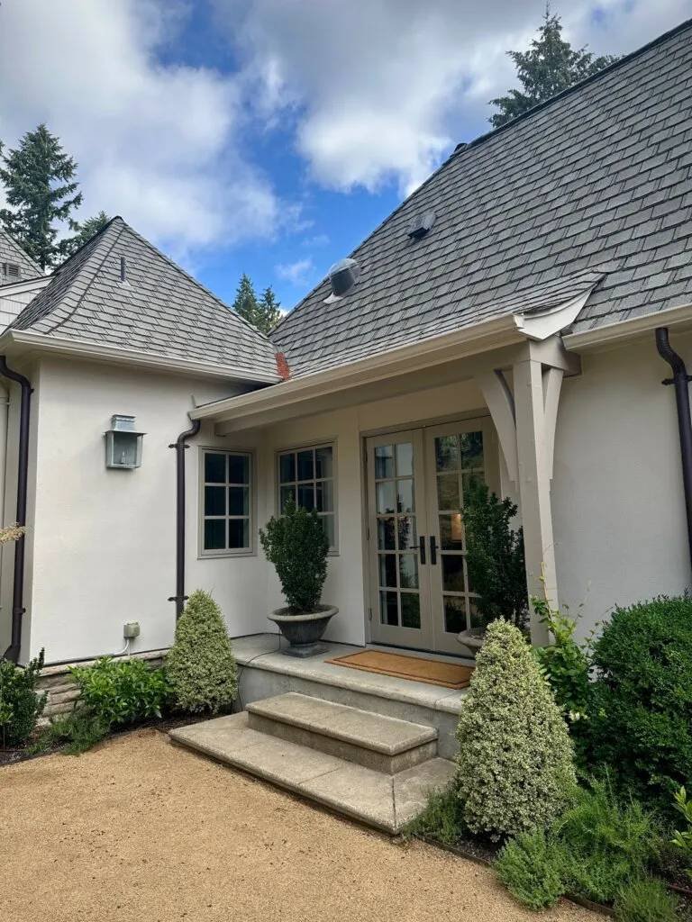 Elegant white luxury home exterior with French doors, manicured landscaping, and cedar shake roof in Lake Oswego