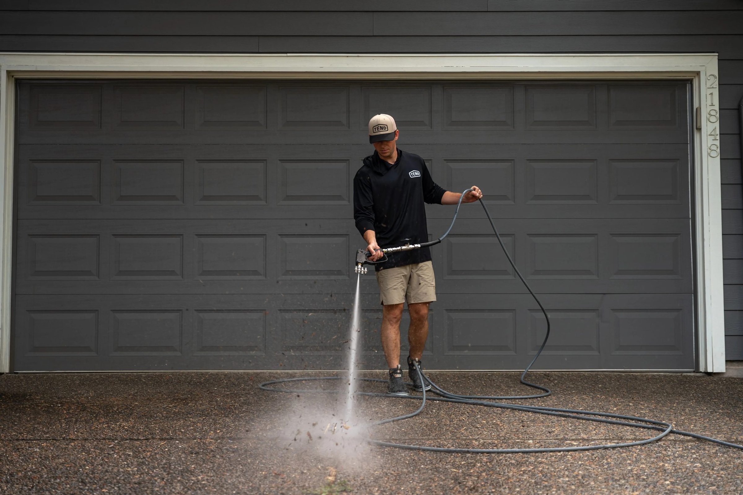 Tend technician pressure washing a driveway in front of a gray garage door