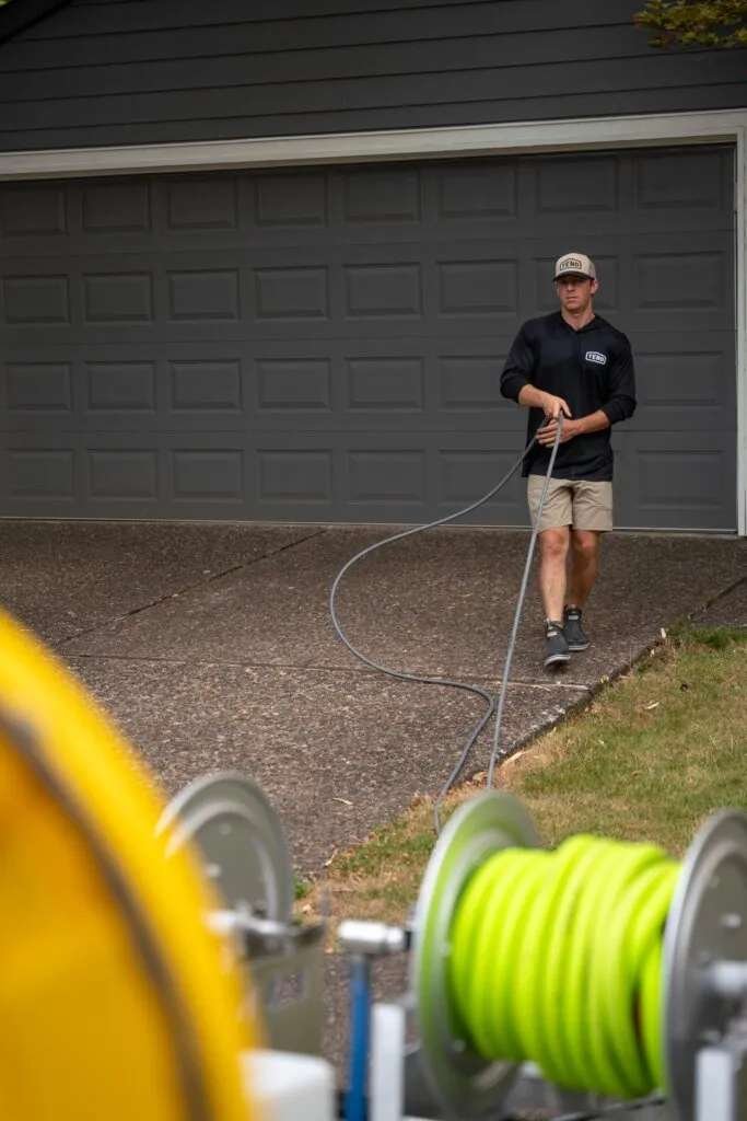 Tend technician walking with hose, professional pressure washing equipment in foreground
